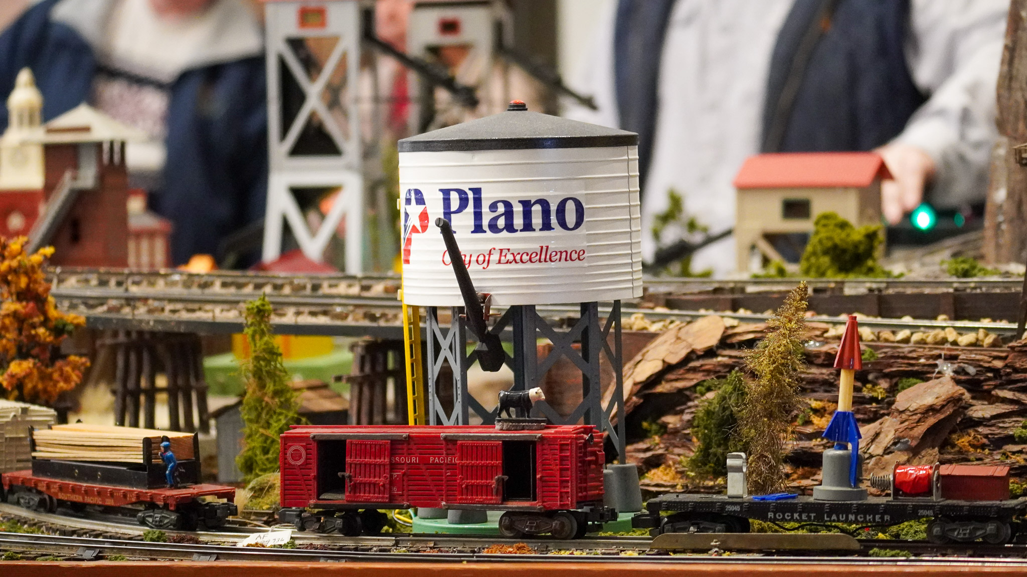 A model train layout with a a train passing by a scenic route showing the Plano, TX water tower.