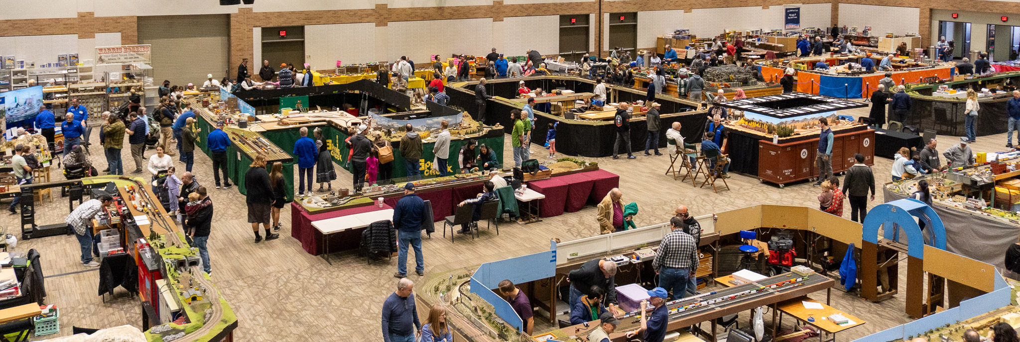 Overview picture of a model train show convention with multiple layouts on display.
